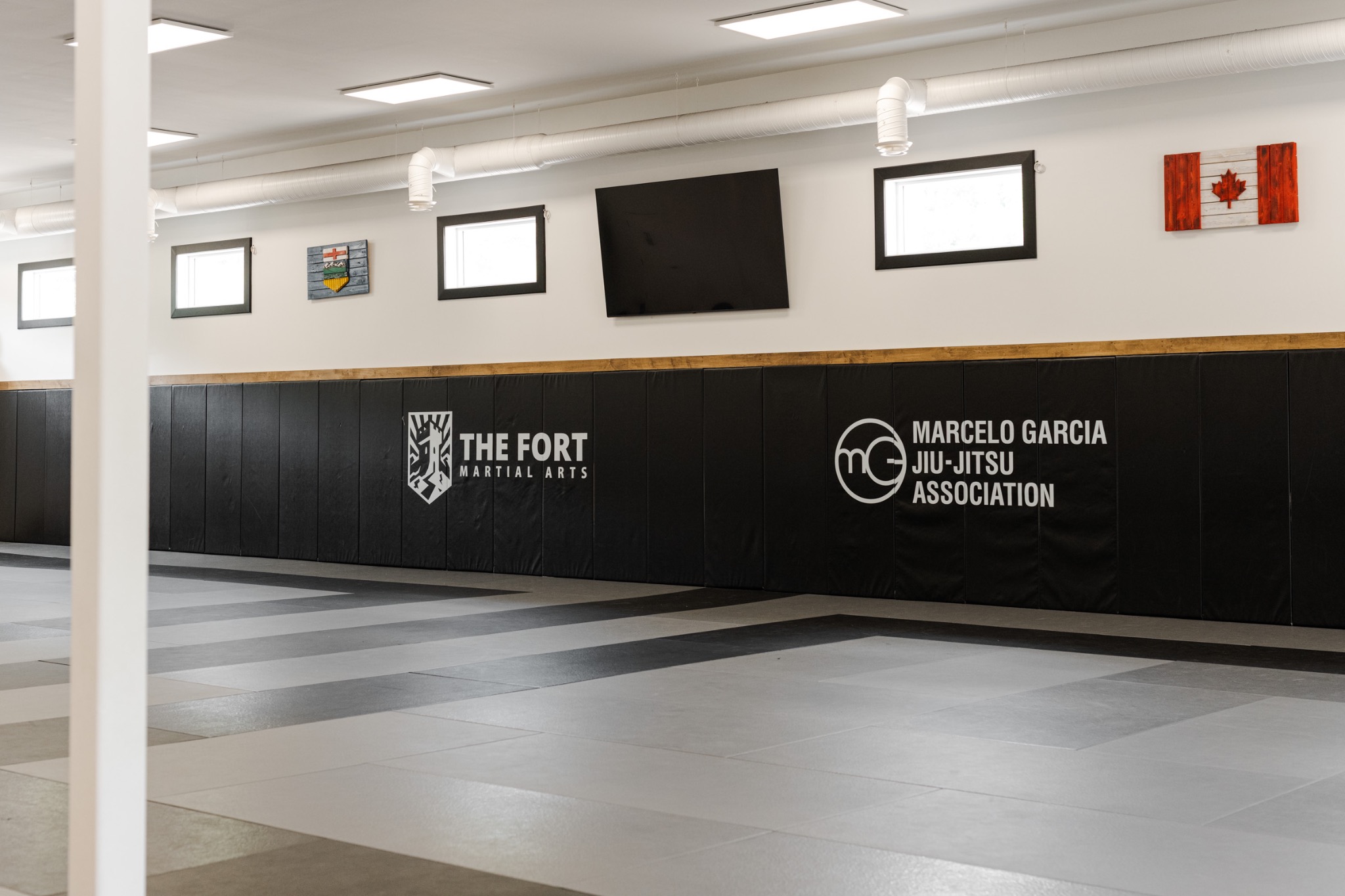 Grey training mats and the padded wall displaying The Fort and Marcelo Garcia Association logos