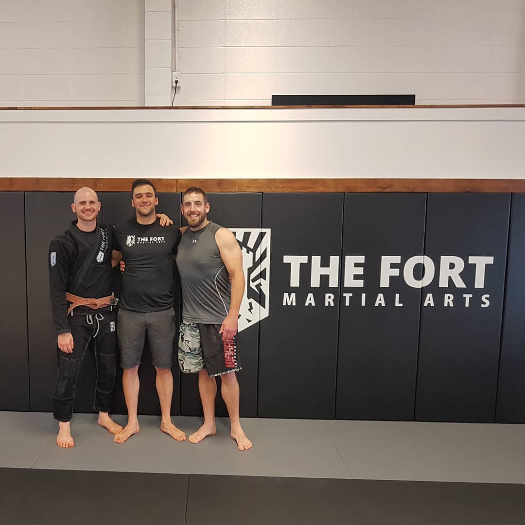 Three teammates standing together in front of the original Fort Martial Arts wall