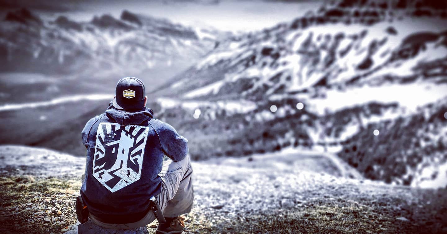 A hiker wearing a hoodie with The Fort crest looks across a snowy mountain landscape.