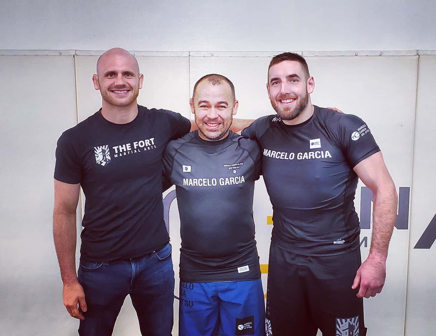 Three martial artists pose together in Fort and Marcelo Garcia training shirts.