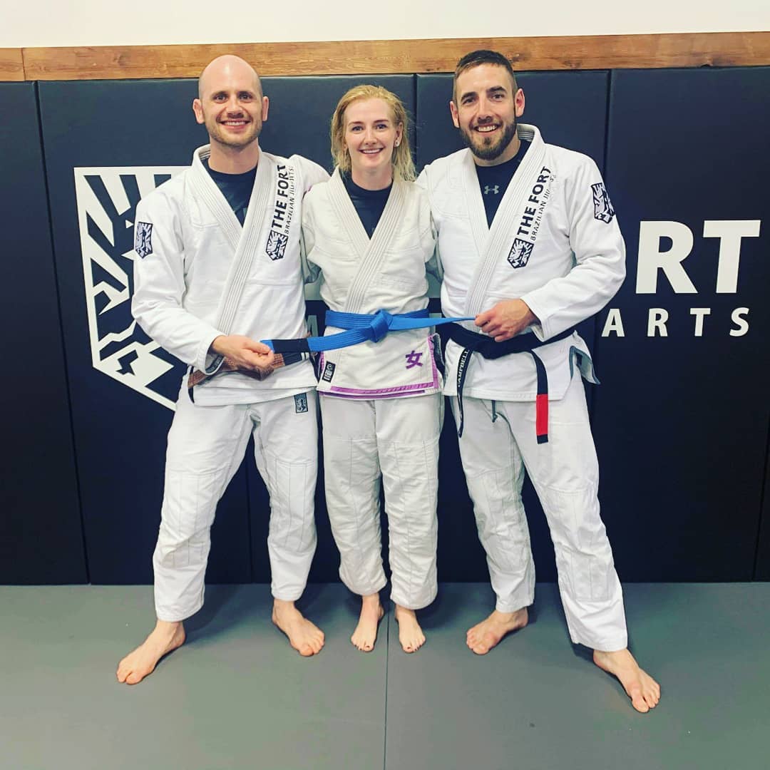 Kelsey Munn wearing her new blue belt between two Fort coaches