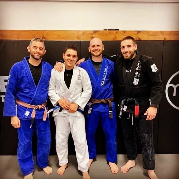 Four Fort members and coaches in gis pose together for a blue-belt promotion.